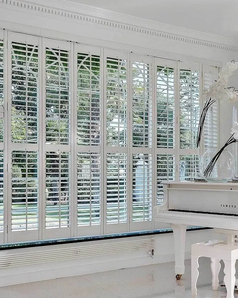 Full-height Seattle range shutters in a conservatory beside a white grand piano
