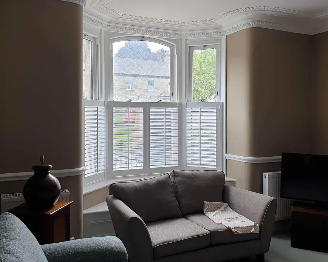 Café style white shutters in a lounge bay window with a grey sofa