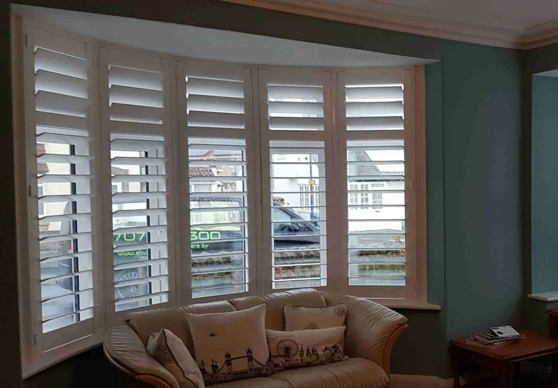 Curved bay shutters behind a cream sofa with cushions