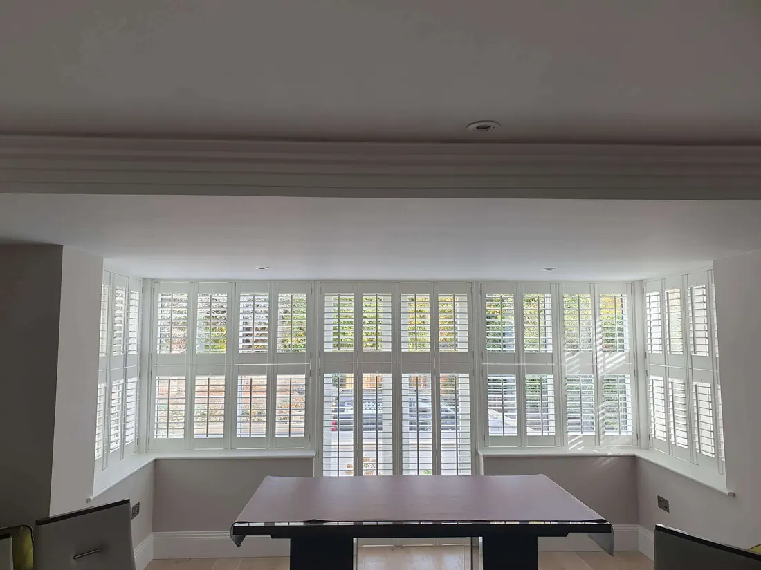 Full height white shutters around a wide square bay in a dining room