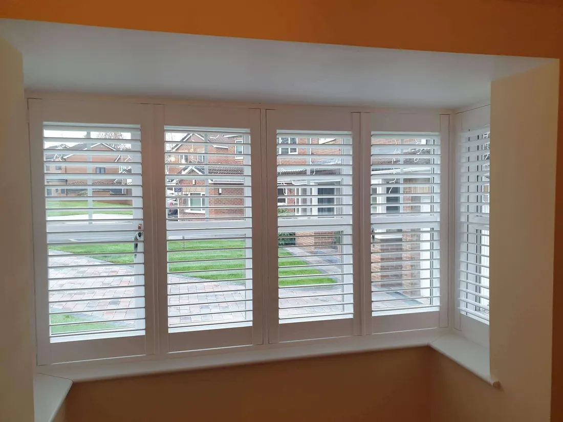 White shutters across a square bay window in a room with an orange wall